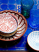 Hand painted bowls on blue tabletop with glasses in Moroccan riad North Africa