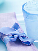 Blaue Schleife auf fliederfarbener Serviette mit Glas