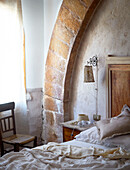 Ungemachtes Bett mit Steinbogen und Holzstuhl Sizilien Italien