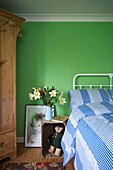 Cut lilies on wooden bedside crate in bright green bedroom of Cranbrook family home, Kent, England, UK