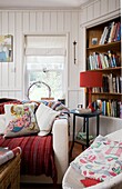 Cushions on sofa at window with bookcase, in Tenterden family home, Kent, England, UK