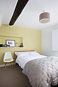 Einzelbett mit grauer Bettdecke in einem gelben Schlafzimmer in einem Cottage mit Holzrahmen