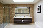 Double basin in brown tiled bathroom with glass shower cubicle in modern home Bath Somerset, England, UK