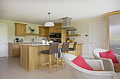 Wicker bar stools at wooden breakfast bar in open plan kitchen living room of contemporary farmhouse in Nuthurst, West Sussex, England, UK