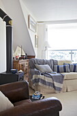 Brauner Ledersessel und Sofa neben dem Holzofen im Wohnzimmer eines Hauses in Dartmouth, Devon, Vereinigtes Königreich