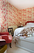 Red chair and patterned wall paper in bedroom of Etchingham farmhouse East Sussex England UK
