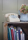 Cremefarbenes Wählscheibentelefon mit Hortensien auf einem hölzernen Bücherregal in einem Bauernhaus in High Halden, Kent, England, UK