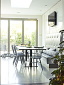 Grey painted chairs at table with bench seat and patio doors in London home England UK