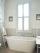 Freestanding bath below shuttered window in bathroom of London home England UK