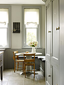 Kitchen table with pew chairs at window in grey painted kitchen East Sussex country house England UK