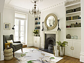 Circular mirror above fireplace with bookshelves in living room with grey armchair North London townhouse England UK