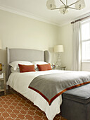 Light grey headboard with burnt ochre velvet cushions and blanket trim in bedroom of North London townhouse England UK