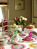 Cut tulips and cakes with teacups on floral patterned tablecloth in dining room of Nottinghamshire home England UK