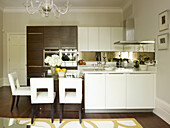 White leather armchairs at glass table in open plan kitchen of Little Venice townhouse London England UK