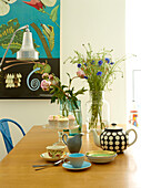 Teapot and cut flowers on wooden table with artwork in London family home, UK