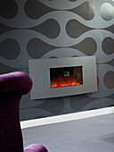 Purple wingback at electric fireside with grey patterned wallpaper in Manchester home, England, UK