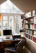 Schreibtisch mit Computer und Stuhl am Fenster mit Bücherregal in Hove home East Sussex UK