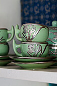 Green teacups with silver ornamentation on shelf in London home UK