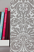 Books on shelf with grey patterned wallpaper in contemporary London home, England, UK