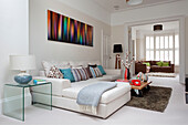 Couchtisch mit Rollen und weißem Sofa unter moderner Kunst in einem Doppelzimmer eines modernen Hauses in London, UK