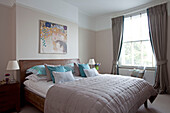 Artwork above wooden double bed with neutral quilt in contemporary London home, UK