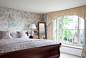 Polished wooden bed in room with toile wallpaper in East Sussex home, England, UK