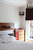 Wooden chest of drawers next to bed with white pillows in London bedroom UK