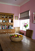 Wooden fruitbowl on table with dresser in pink Suffolk dining room UK