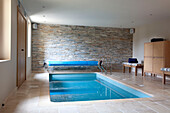 Swimming pool with exposed stone wall in Cotswolds home UK