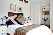 Patterned cushions on bed with carved headboard in white bedroom in London townhouse, England, UK