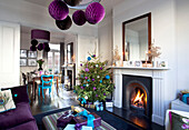 Christmas tree with purple decorations and lit fire in double room of Victorian London home, UK