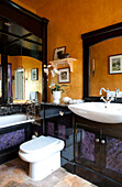 White ceramic basin and toilet in purple and yellow Surrey bathroom with gloss black mirror frames, England, UK