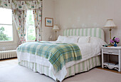 Grüne Schottenkaro-Decke auf einem Doppelbett mit gestreiftem Kopfteil und Volant in einem Landhaus in Sussex, England, UK
