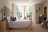 Sonnendurchflutetes Schlafzimmer mit großem gepolsterten Kopfteil und Naturfaserteppich in einem Landhaus in Sussex England UK