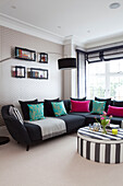 Pink and turquoise cushions on black sofa with striped ottoman in contemporary Surrey country home England UK