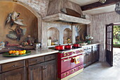 Red range oven and casserole dishes with wall fresco in kitchen of French holiday villa