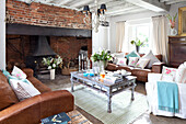 Braune Ledersofas und Couchtisch im Wohnzimmer mit offenem Kamin aus Backstein in einem Haus in West Sussex, England, UK