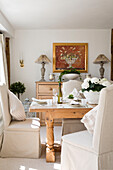 Slip covered dining chairs at table with gilt-framed artwork in West Maling dining room, Kent, England, UK