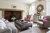 Sesselpaar und Ottomane mit offenem Ziegelsteinkamin im Wohnzimmer eines Londoner Hauses England UK