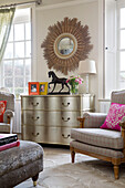 Sunburst mirror above silver chest of drawers in living room of London home England UK