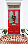 Weihnachtsgirlande an der leuchtend roten Eingangstür eines Londoner Hauses, England, Vereinigtes Königreich