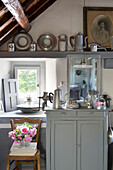 Pewter homeware and cut flowers with grey painted side unit at window in French farmhouse