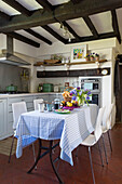 White chairs with gingham tablecloth in beamed kitchen of Camber cottage East Sussex England UK