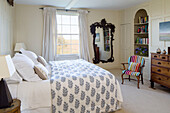 Leaf motif bed cover in bedroom with decorative mirror and striped armchair in Camber cottage East Sussex England UK