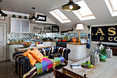Chesterfield sofa under skylight windows in open plan attic kitchen with mirrored splashback in London home, England, UK