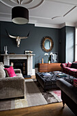 Grey buttoned ottoman and sofa with vintage mirror and antlers in Sussex living room, England, UK