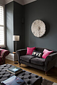 Dunkelgraues Zweisitzer-Sofa mit geknöpfter Ottomane und Federschmuck in einem modernen Wohnzimmer in Sussex, England, Vereinigtes Königreich