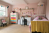Einzelbett mit Schreibtisch und bemalten Schubladen in einem pastellrosa Mädchenzimmer in einem Londoner Haus, England, UK