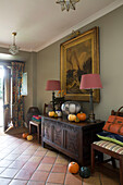 Pair of lamps on carved sideboard with gilt-framed artwork in hallway of London home,  England,  UK