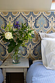 Cut flowers on bedside table with patterned headboard in UK farmhouse